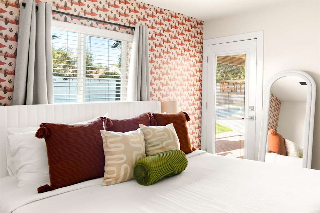The Sunkiss — bedroom with cactus patterned wallpaper, white headboard, decorative pillows, and glass door leading outside