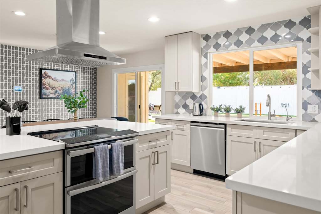 The Sunkiss — kitchen with stainless steel double oven in the island, range hood, and window overlooking backyard
