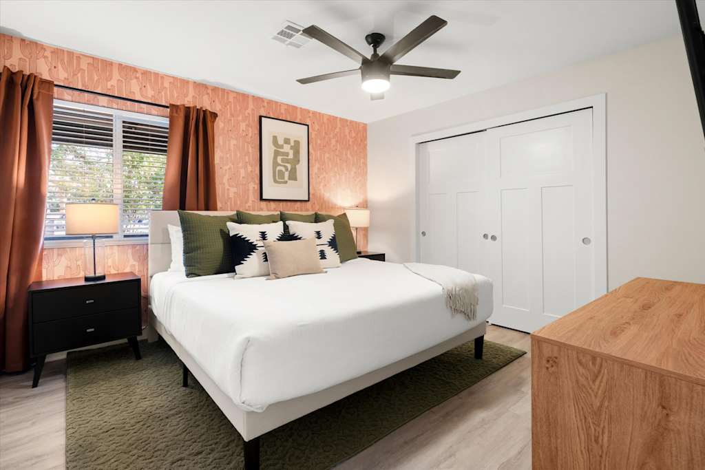 The Sunkiss — bedroom with large bed, patterned pink wallpaper accent wall, ceiling fan, and sliding closet doors