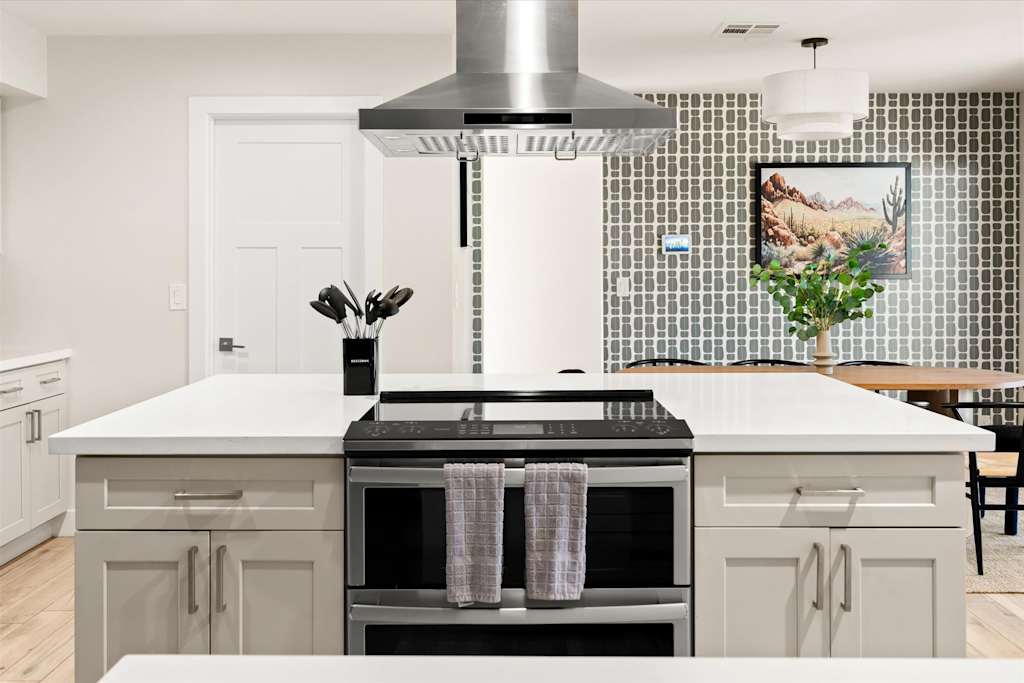 The Sunkiss — kitchen island with electric cooktop range and stainless steel exhaust hood against accent wall
