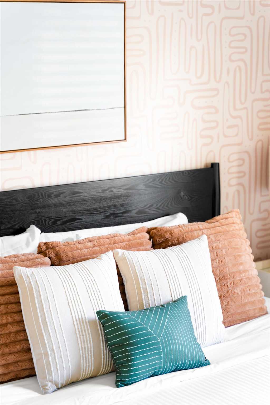 The Sunkiss — bed with black wood headboard, patterned wallpaper, and textured white, rust, and green pillows