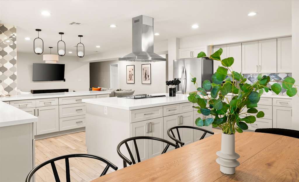 The Sunkiss — open kitchen and dining space with island, stainless steel hood, white cabinets, and wooden table