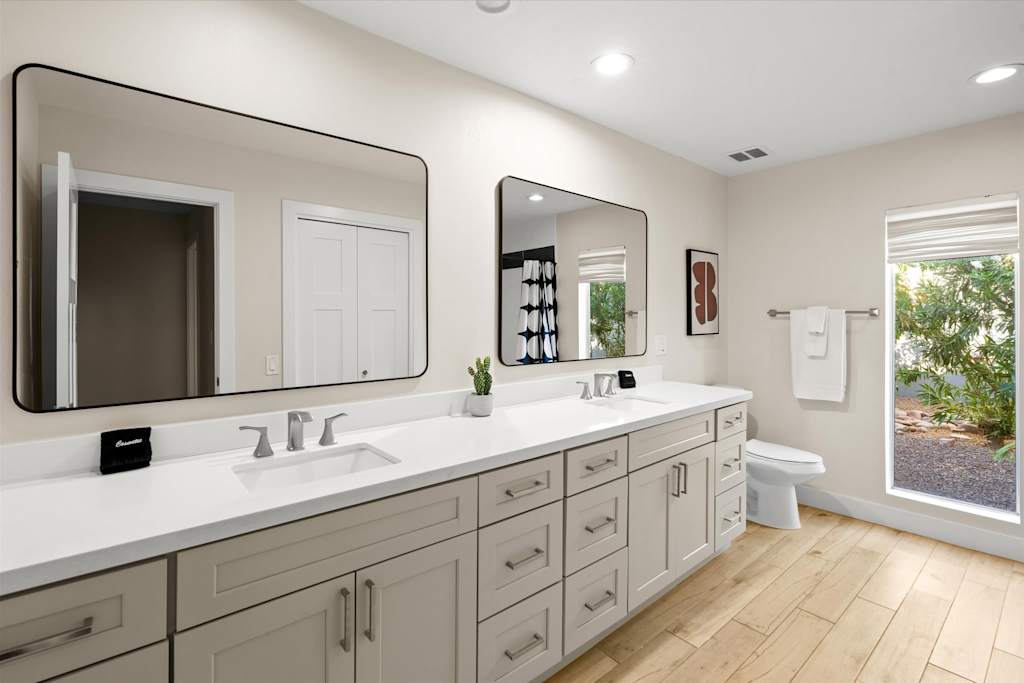 The Sunkiss — spacious bathroom with double vanity, two large mirrors, white countertop, and light wood flooring