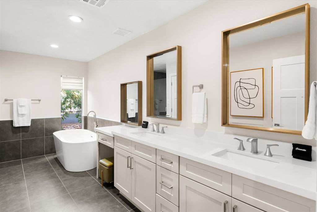 The Sunkiss — spacious bathroom featuring a double vanity, three gold-framed mirrors, and a freestanding soaking tub