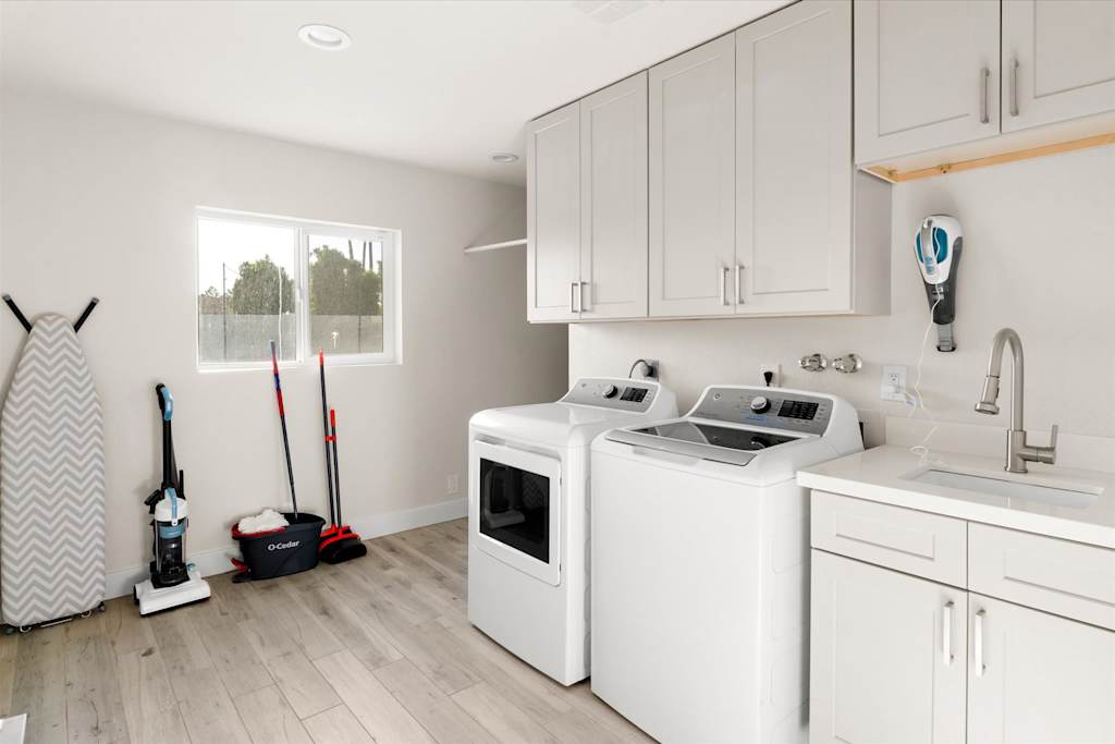 The Sunkiss — laundry room equipped with a washer, dryer, sink, white cabinetry, and an ironing board