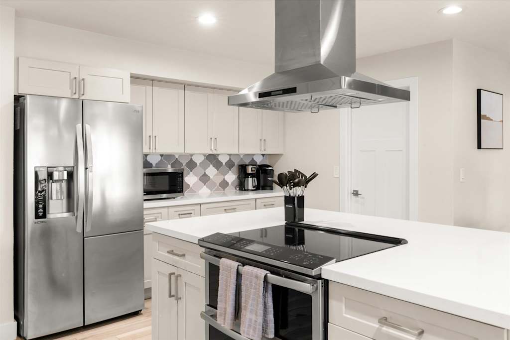 The Sunkiss — kitchen featuring white cabinetry, stainless steel refrigerator, range hood, and island with cooktop