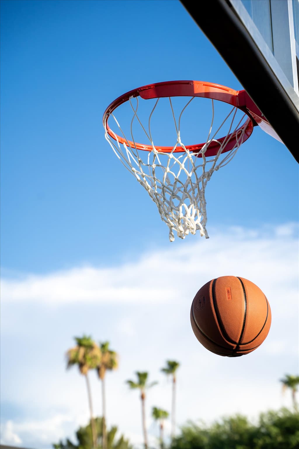 The Sunkiss — low-angle shot of a basketball hoop and ball in midair against a blue sky