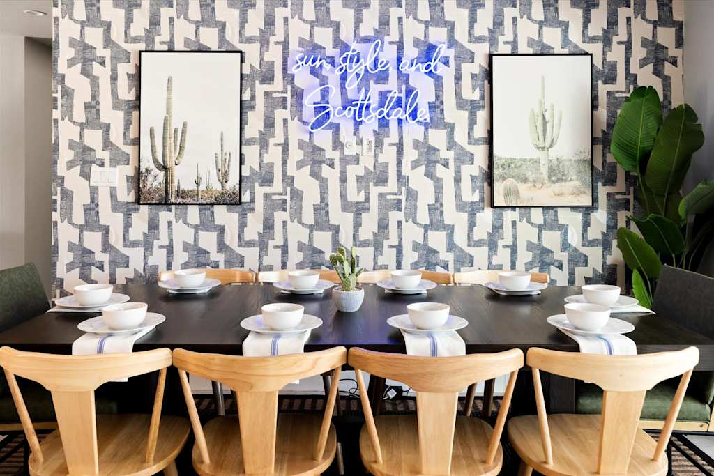 The Scottsdale Social — dining room with long table, modern wooden chairs, cactus art prints, and decorative neon sign