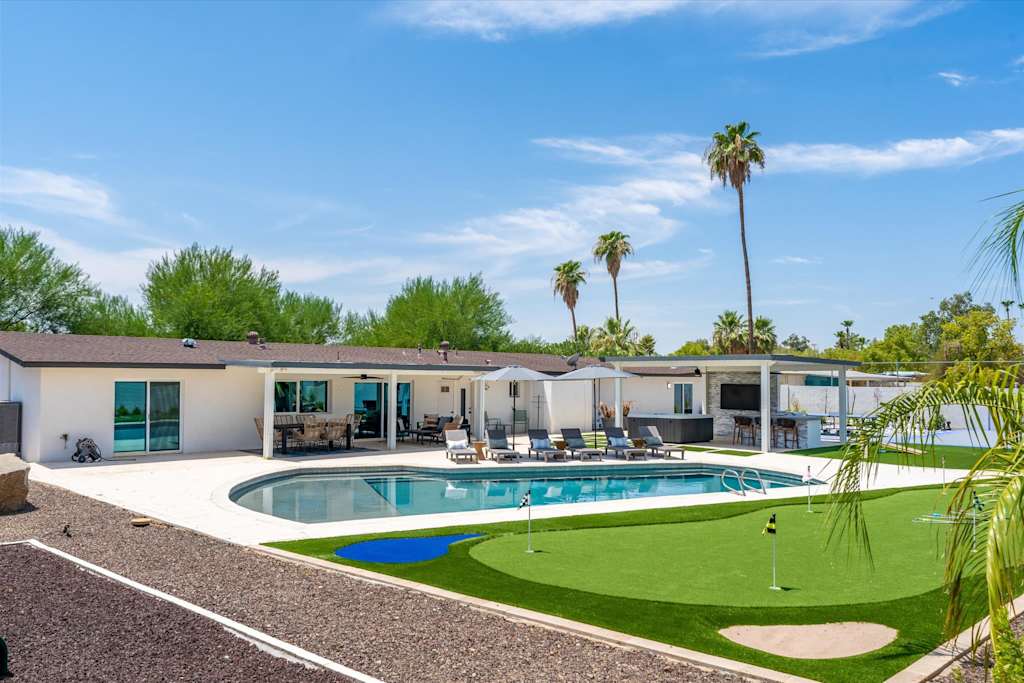 The Scottsdale Social — backyard with a swimming pool, putting green, covered patio, and palm trees under a blue sky