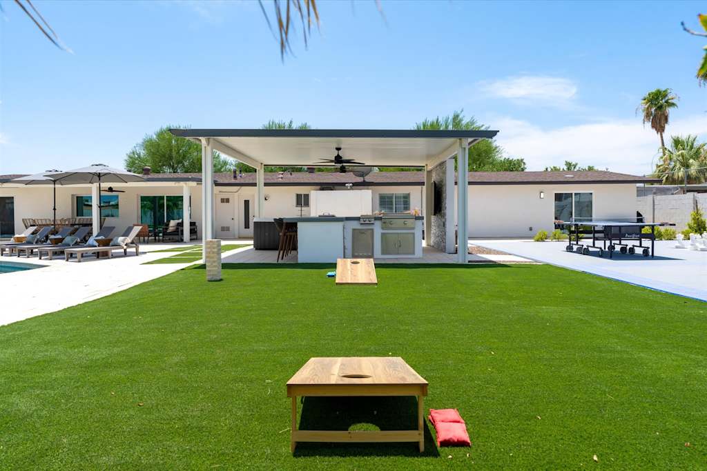 The Scottsdale Social — backyard lawn with cornhole boards, an outdoor kitchen pavilion, and a ping-pong table