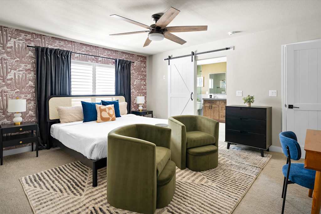The Scottsdale Social — bedroom with a patterned accent wall, bed, two green armchairs, and sliding barn door to bathroom