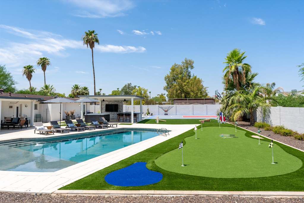 The Scottsdale Social — backyard with a large putting green, swimming pool, lounge chairs, and covered outdoor bar area