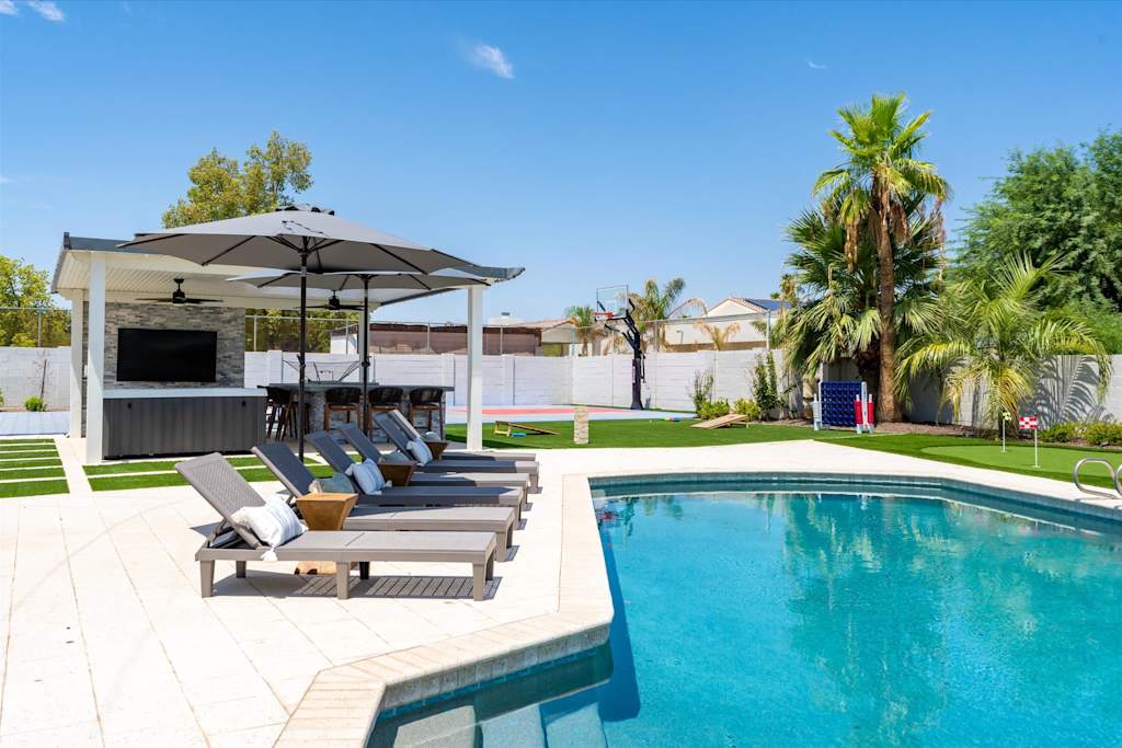 The Scottsdale Social — backyard swimming pool with lounge chairs, covered patio with outdoor tv, and palm trees