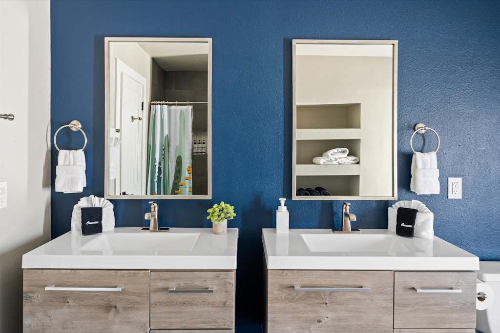 The Scottsdale Social — bathroom double vanity with wood grain cabinets, two rectangular mirrors, and a blue wall