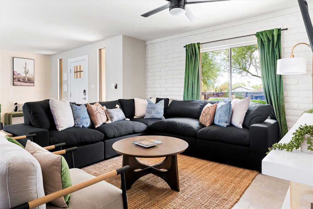 The Scottsdale Social — living room with black sectional sofa, decorative pillows, round coffee table, and white brick wall