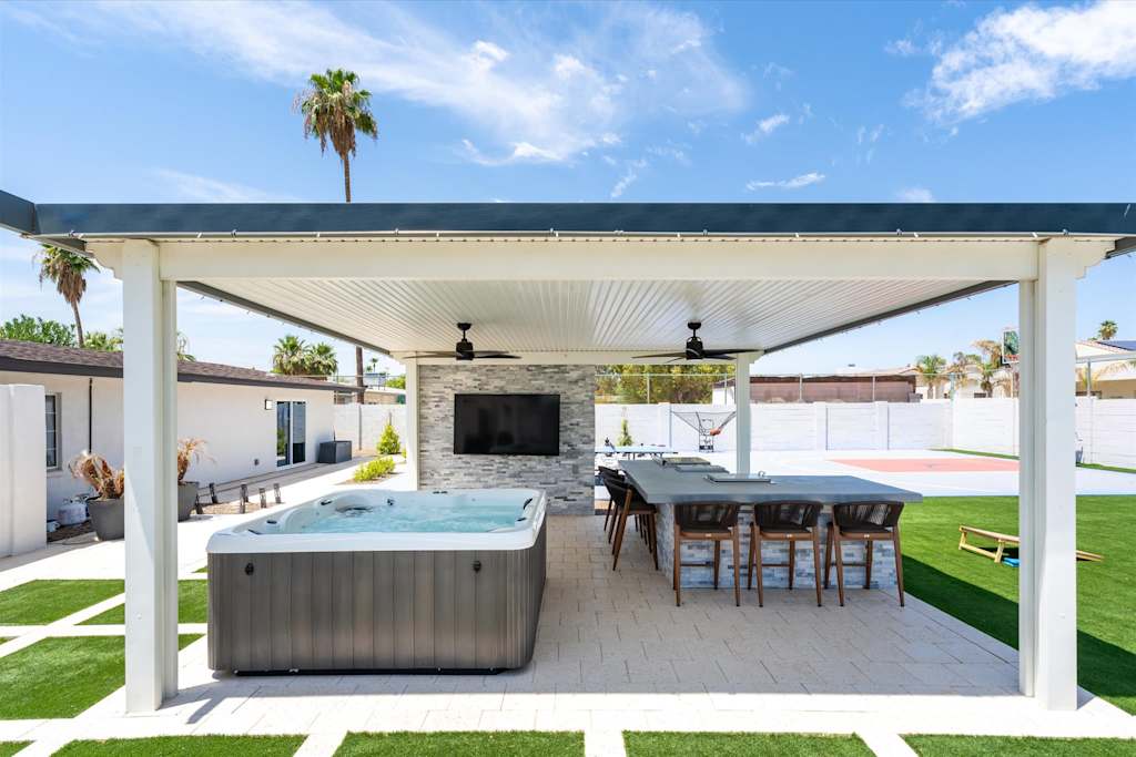 The Scottsdale Social — covered outdoor pavilion with hot tub, bar seating, wall-mounted television, and backyard view