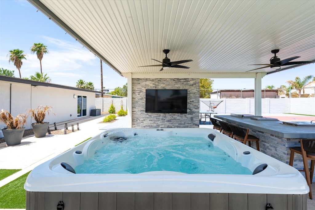 The Scottsdale Social — covered outdoor patio featuring a hot tub, mounted television on a stone wall, and bar seating
