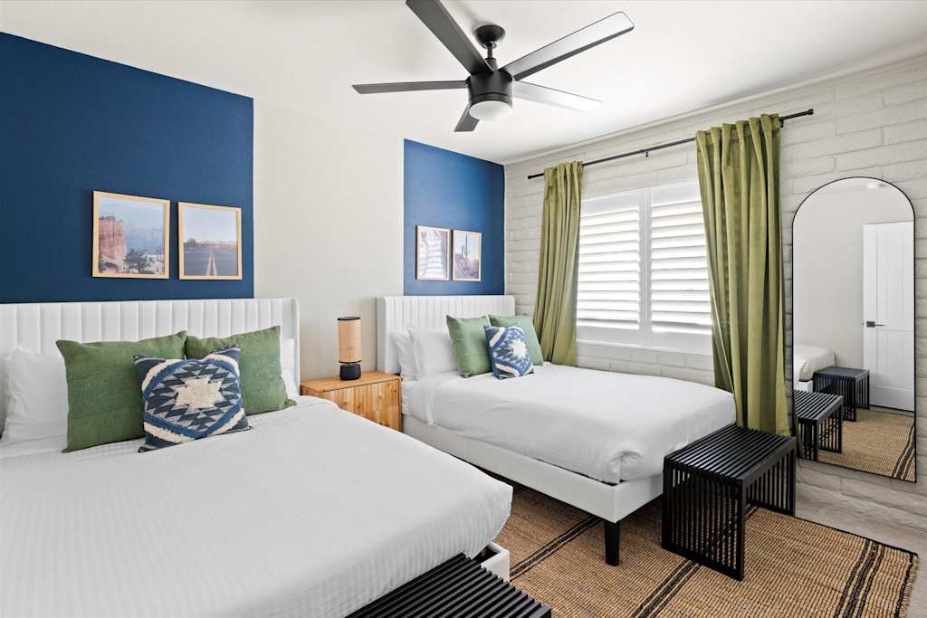 The Scottsdale Social — bedroom with two beds, navy accent wall sections, arched mirror, and woven area rug