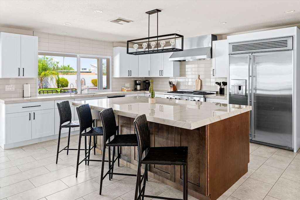 The Scottsdale Social — spacious kitchen with large island, black barstools, white cabinetry, and stainless steel refrigerator