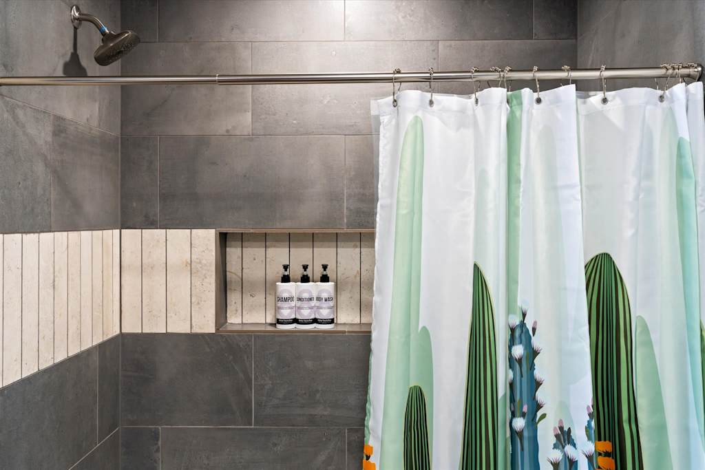 The Scottsdale Social — shower with dark gray wall tiles, recessed niche for toiletries, and cactus-print shower curtain