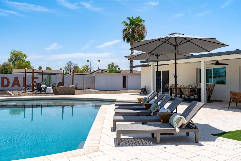 The Scottsdale Social — backyard patio with swimming pool, lounge chairs under umbrellas, and covered outdoor seating area