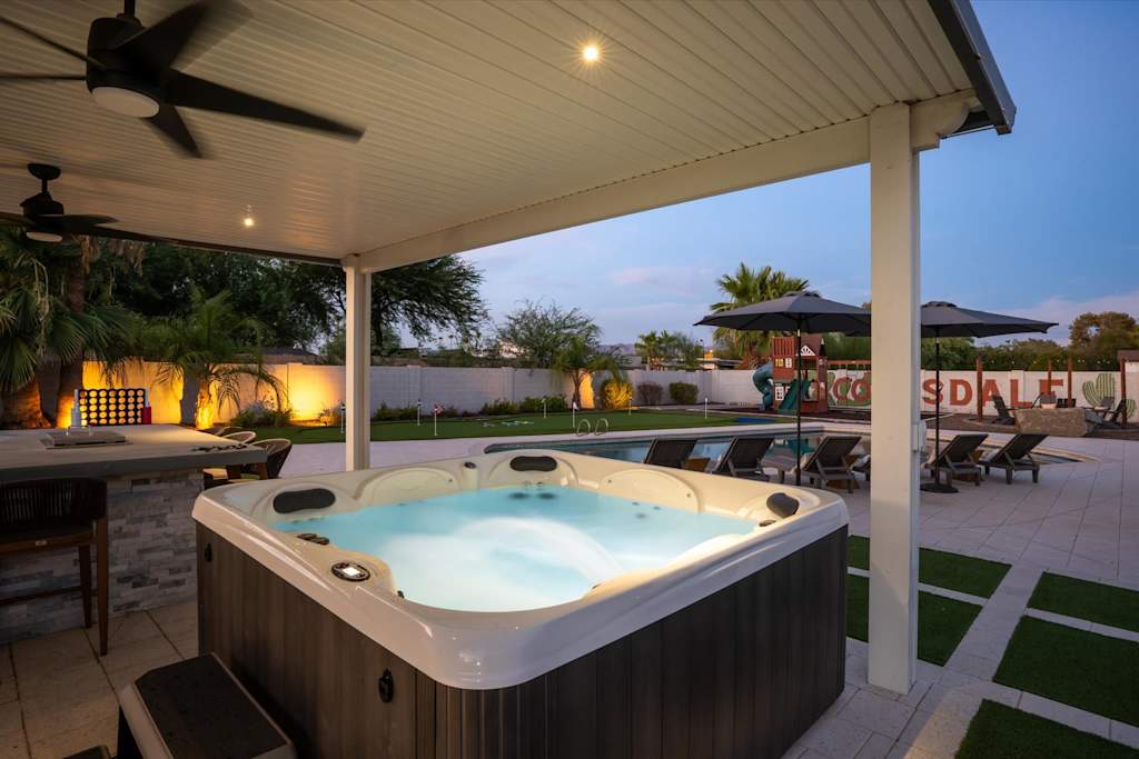 The Scottsdale Social — illuminated hot tub beneath a covered patio overlooking a backyard pool and lounge area