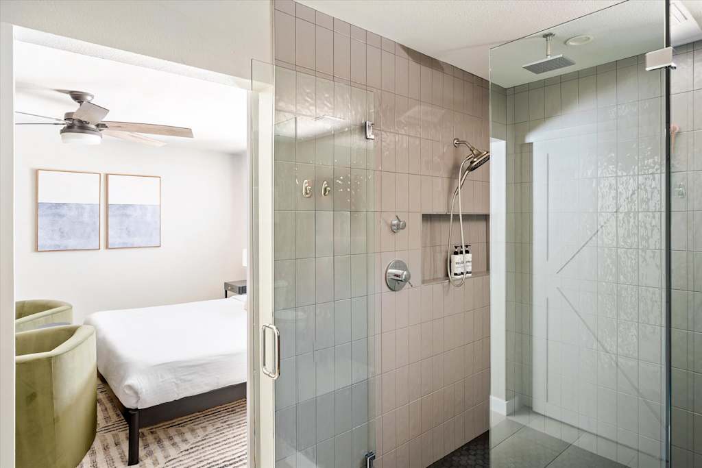 The Scottsdale Social — view from a tiled shower through glass door into a bedroom with a bed and chairs