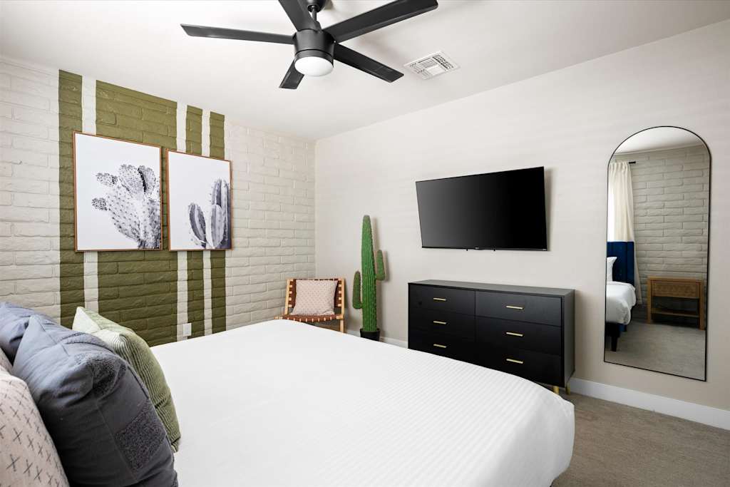 The Scottsdale Social — bedroom with white bed, wall-mounted television, black dresser, arched floor mirror, and painted brick wall