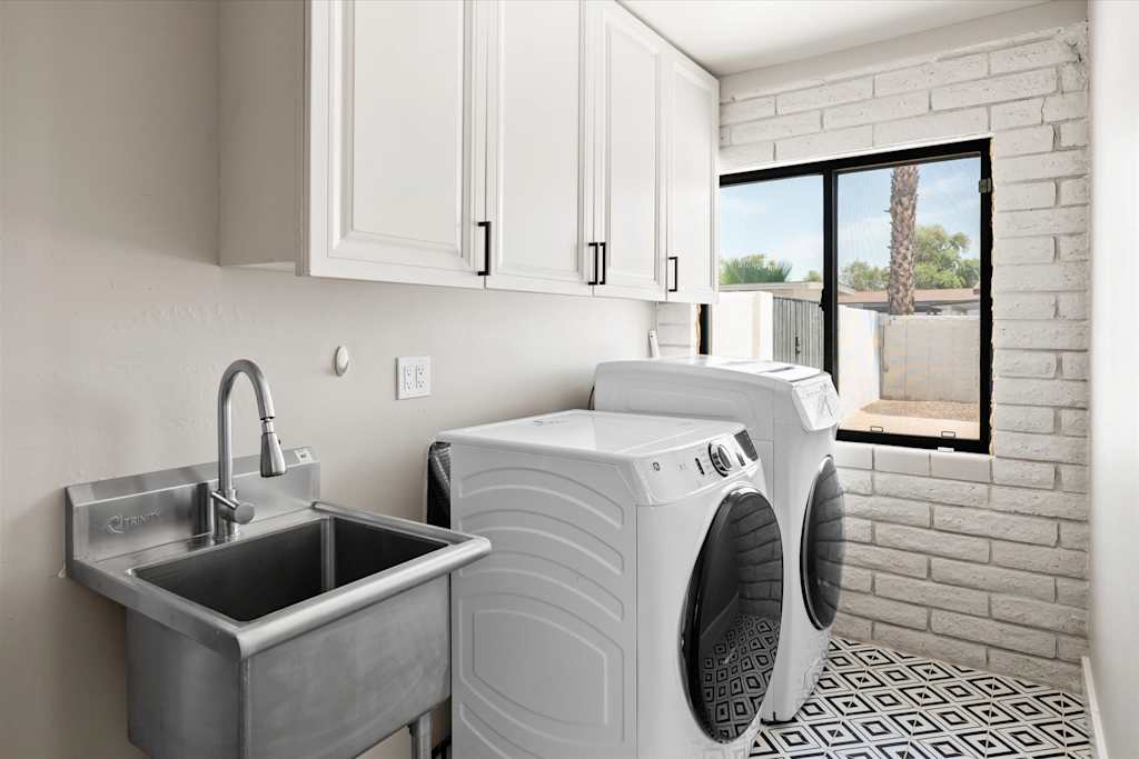 The Scottsdale Social — laundry room with stainless steel utility sink, front-load washer and dryer, and white cabinetry