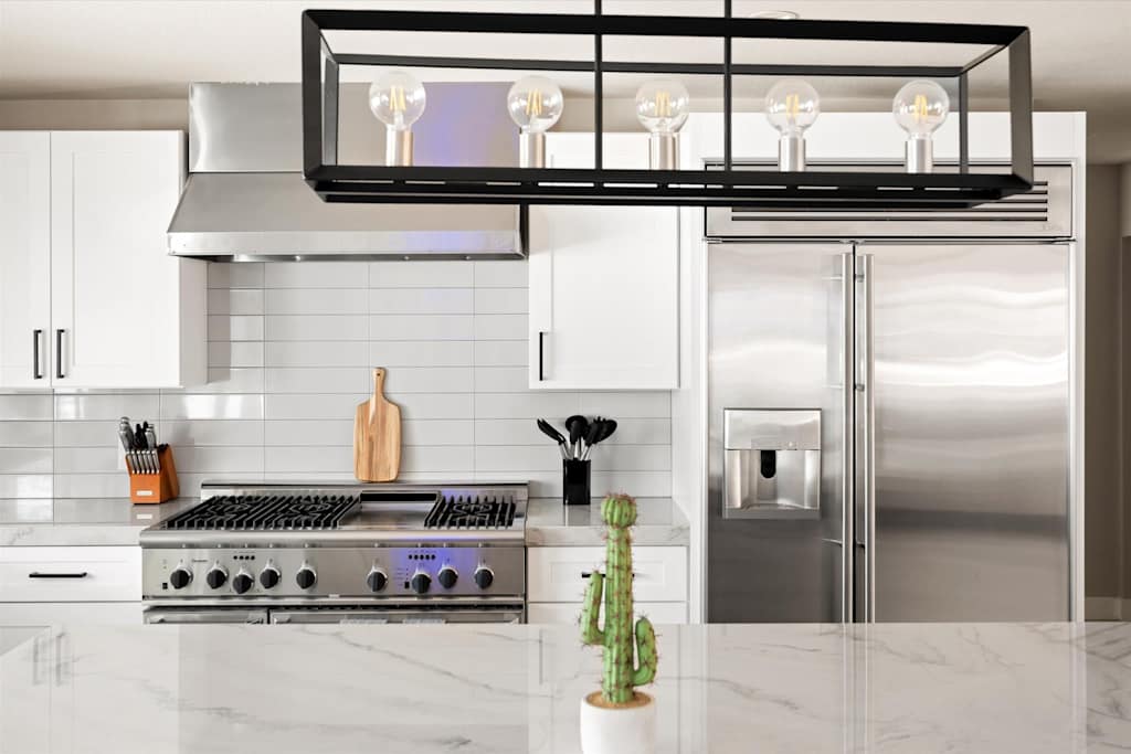 The Scottsdale Social — kitchen with stainless steel appliances, modern rectangular chandelier, white cabinets, and marble island