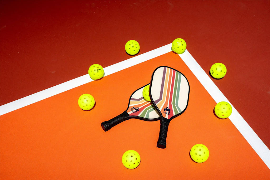 The Sunkiss — two pickleball paddles surrounded by neon yellow pickleballs on a sport court surface