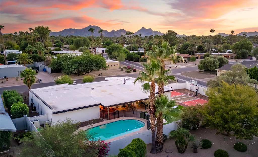 The Sunkiss — aerial view of the backyard swimming pool and sports court with mountains in the background at sunset