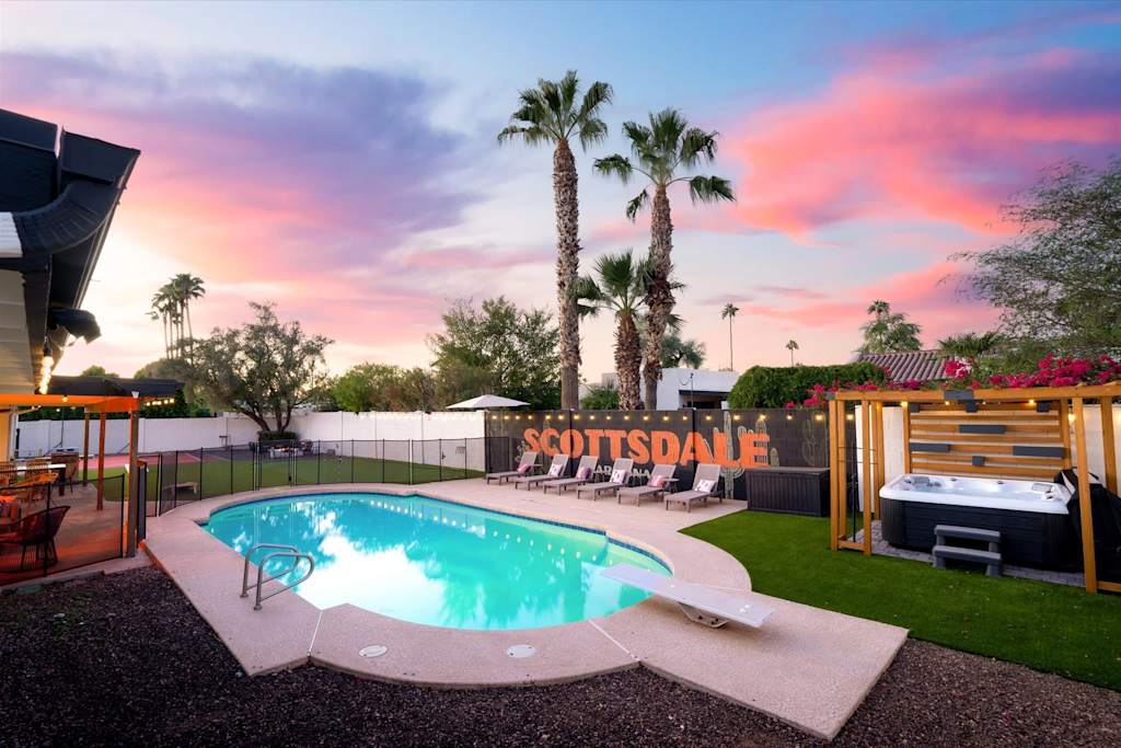 The Sunkiss — backyard pool, hot tub under a pergola, lounge chairs, and palm trees at dusk