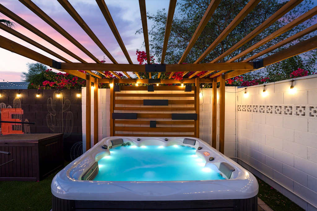 The Sunkiss — illuminated hot tub beneath a wooden pergola with string lights at twilight