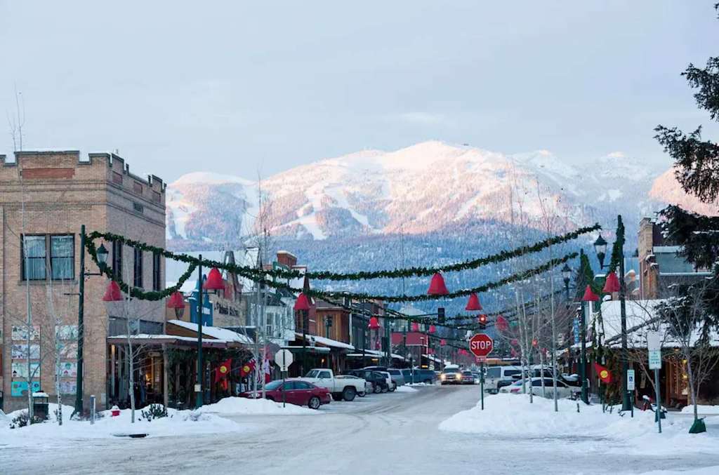 The Evergreen — snow-covered town street decorated with holiday garlands and snowcapped mountains in the background