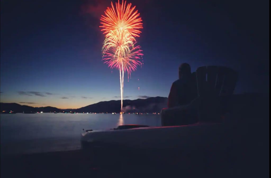 The Evergreen — fireworks exploding over a lake at dusk with a person sitting in the foreground