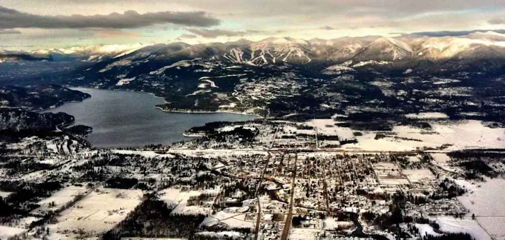 The Evergreen — aerial view of a snow-covered town, lake, and mountain range in winter
