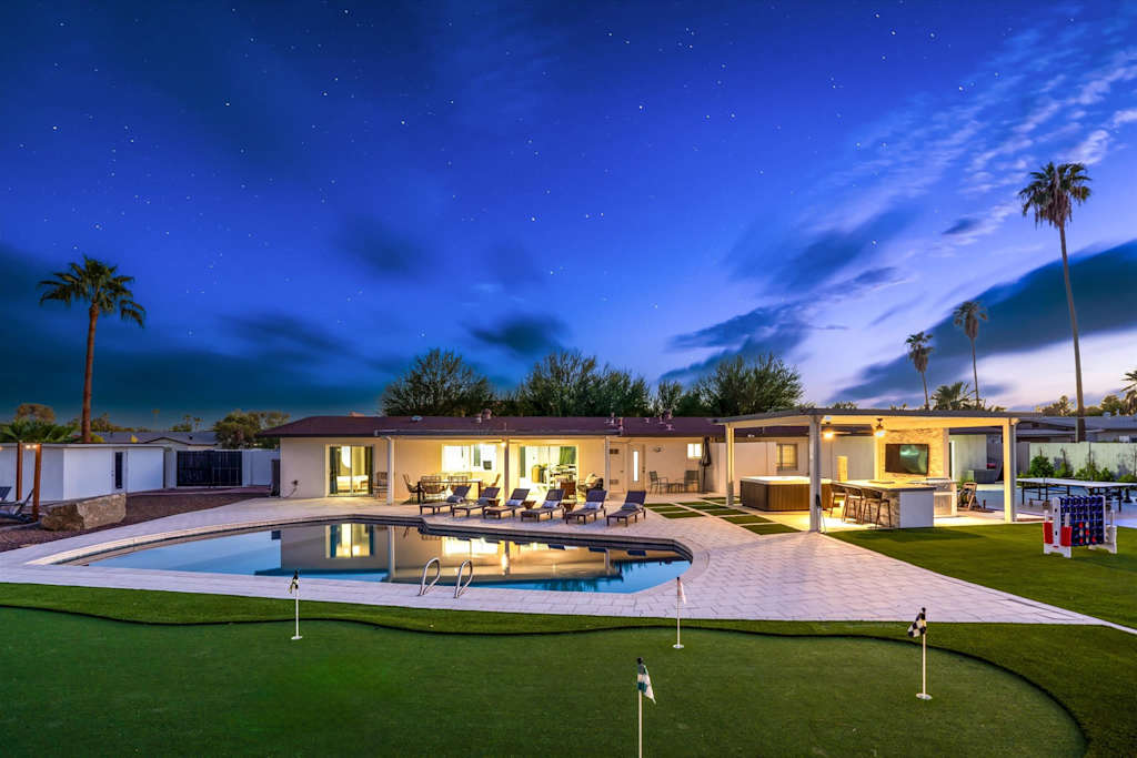 The Scottsdale Social — backyard at night with an illuminated swimming pool, putting green, and covered outdoor seating area