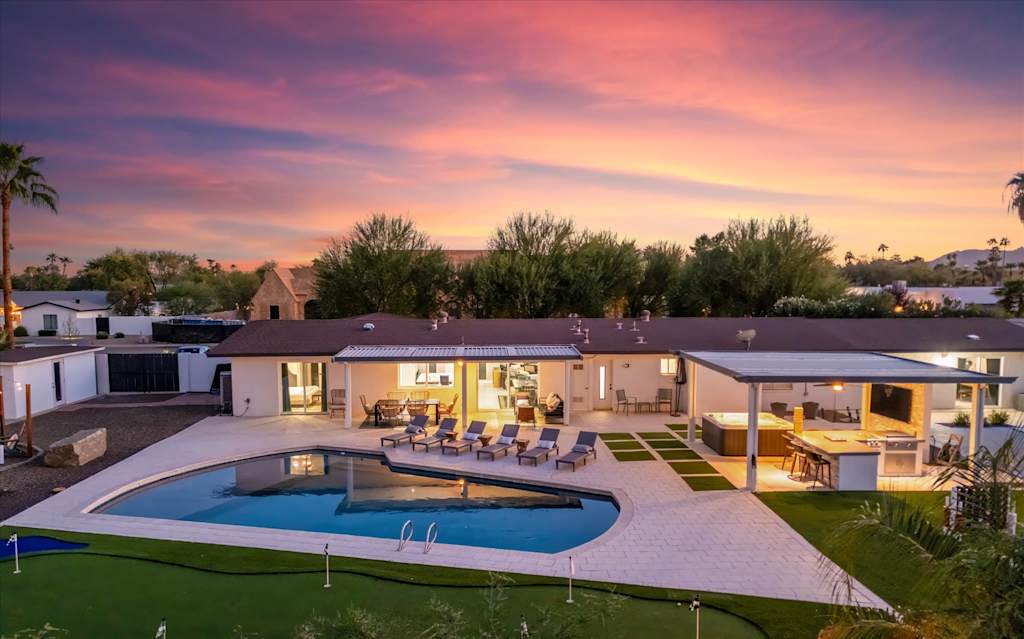 The Scottsdale Social — backyard patio with swimming pool, lounge chairs, covered outdoor kitchen, and putting green at sunset