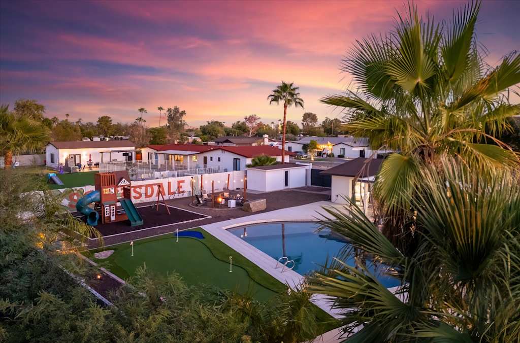 The Scottsdale Social — backyard featuring a children's playset, putting green, and swimming pool seen past palm tree fronds