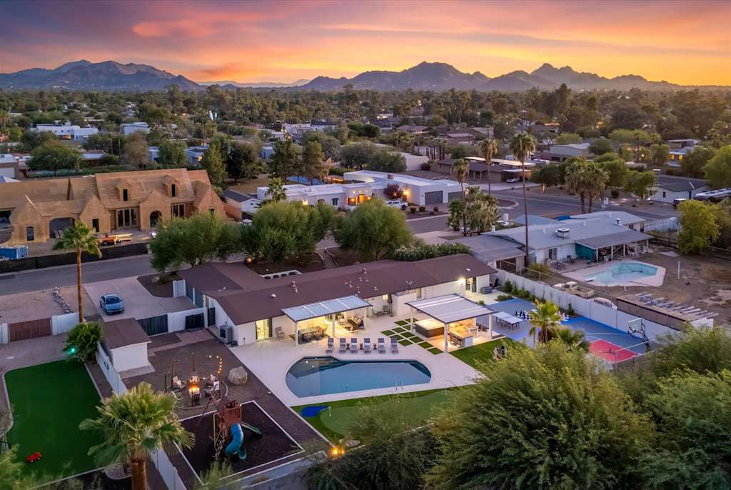 The Scottsdale Social — aerial shot of the house and expansive backyard with mountains under a colorful sunset sky