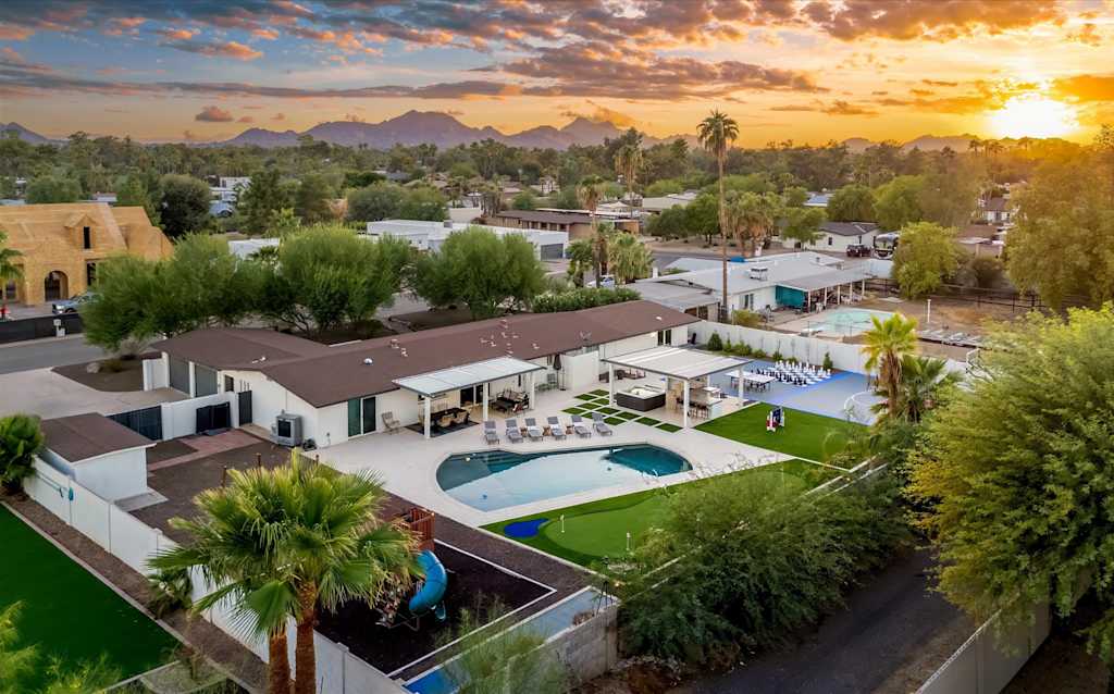 The Scottsdale Social — elevated view of a single-story home with swimming pool, covered patios, and mountain sunset backdrop