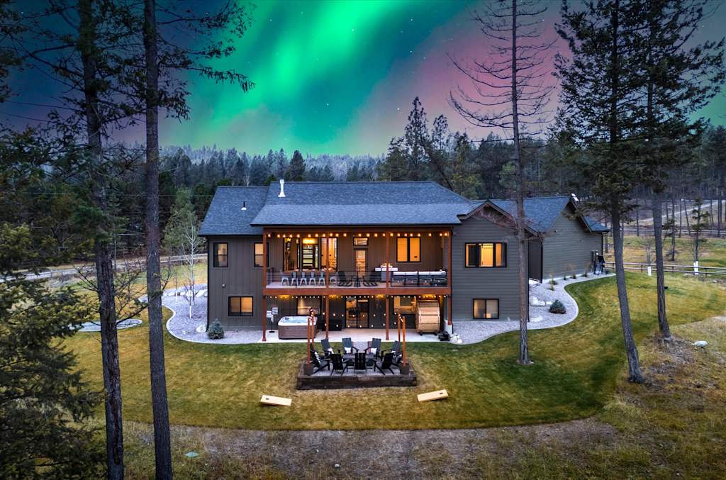The Evergreen — elevated view of the back of a house with illuminated patio and northern lights sky