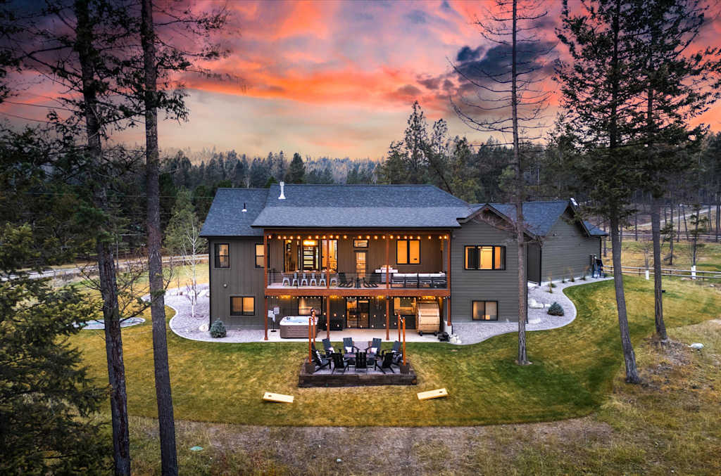 The Evergreen — rear exterior view of a multi-story home at sunset with a patio, deck, and fire pit