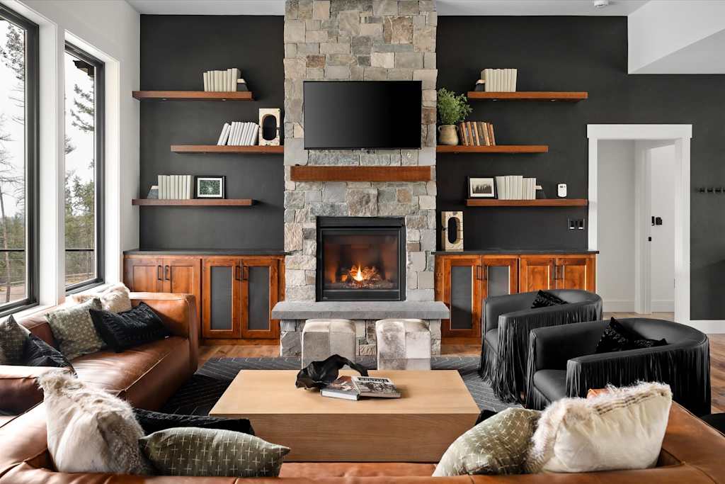 The Evergreen — living room featuring a stone fireplace, mounted television, wooden open shelving, and leather seating