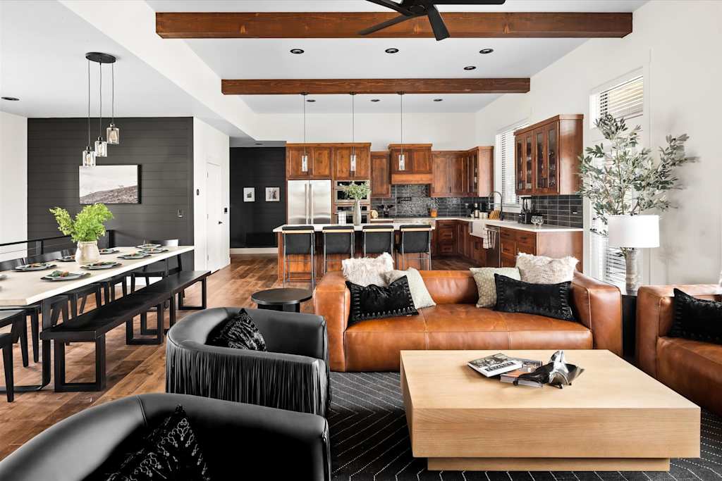 The Evergreen — open-concept living space with a dining table, leather sofa, coffee table, and background kitchen