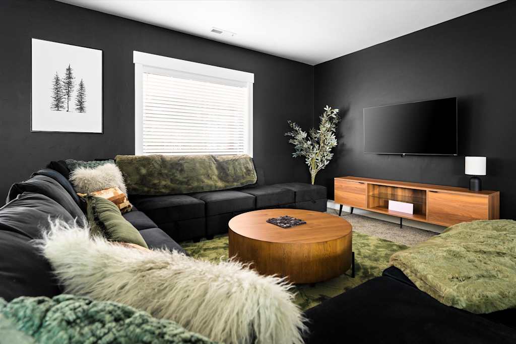 The Evergreen — living room with black walls, large sectional sofa, round wooden coffee table, and wall-mounted tv