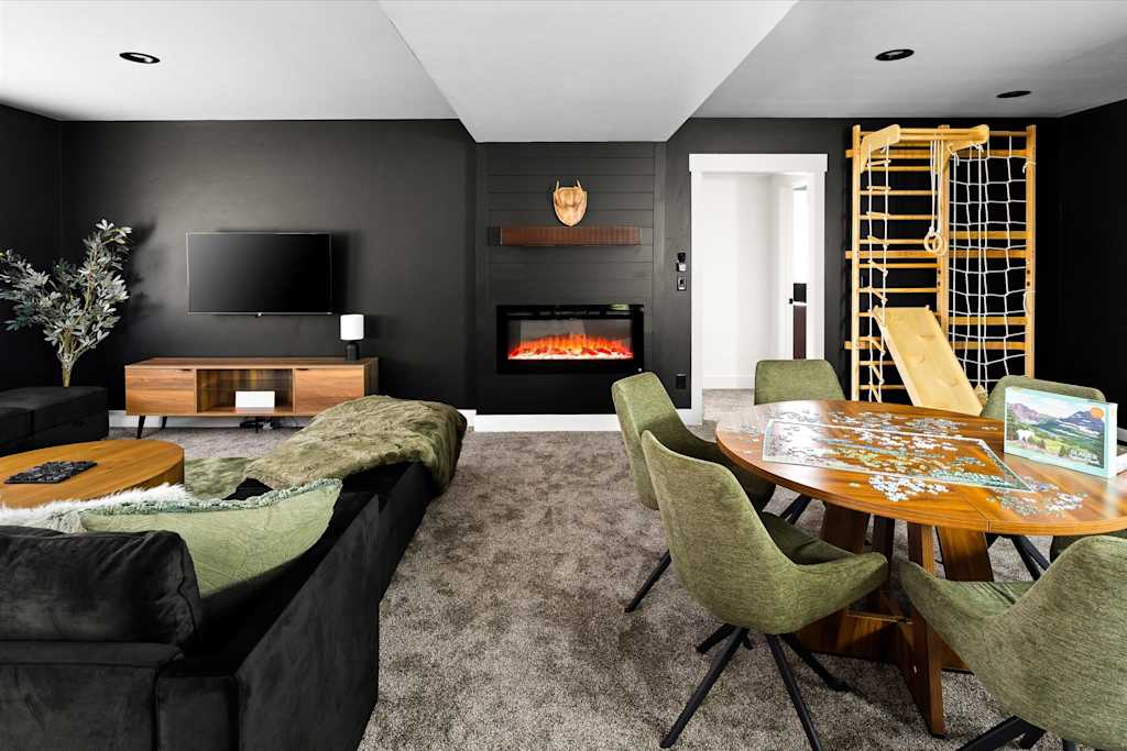 The Evergreen — recreation room with seating area, puzzle table, wall-mounted fireplace, tv, and wooden indoor climbing frame