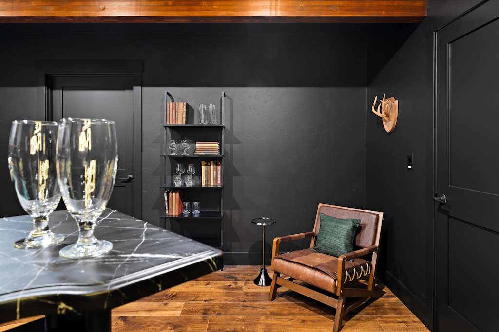 The Evergreen — corner sitting area with black walls, armchair, metal bookshelf, and marble-top table with glasses
