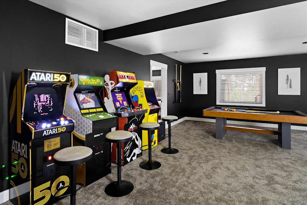 The Evergreen — game room with four classic arcade machines, bar stools, and a pool table on carpeted flooring